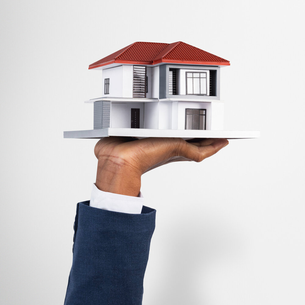 A hand holding a small scale model of a house with a red roof.