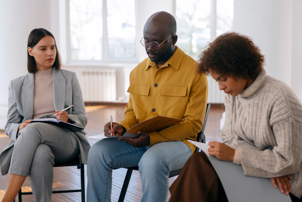 Three people sitting with notebooks and forms, reading through them together.