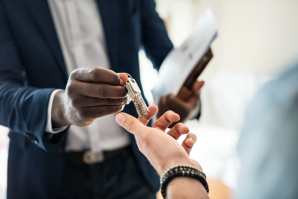 One person handing a set of house keys to another, a folder held under one arm.