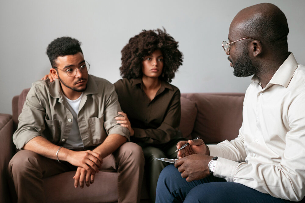Three people sitting together on a sofa, one of them taking notes during the conversation.
